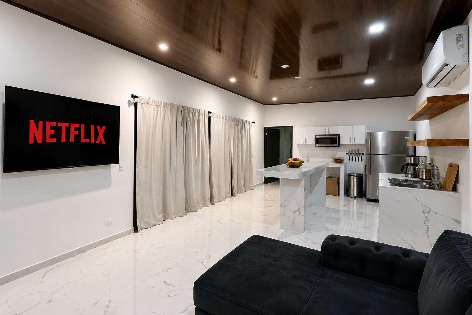 A modern living room with a flat-screen TV, a black sofa, and a kitchen area with a microwave and refrigerator.