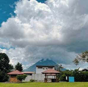 A building with a red roof, a covered outdoor seating area, and a mountain in the background. - Fantastic 3-bedroom house with AC in Provincia de Alajuela (Provincia de Alajuela)
