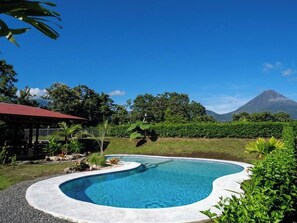 A swimming pool with a curved edge, surrounded by greenery and a mountain in the background. - Fantastic 3-bedroom house with AC in Provincia de Alajuela (Provincia de Alajuela)