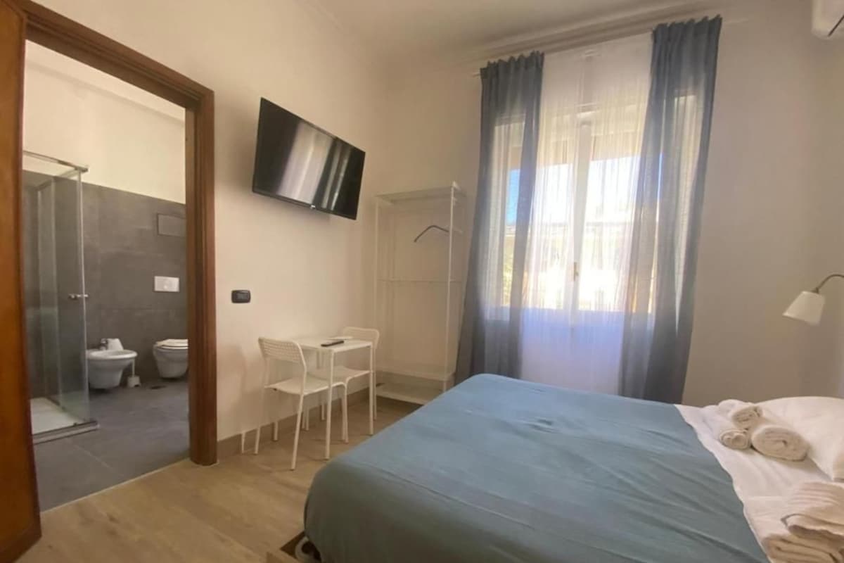 Een hotelkamer met een bed, een televisie, een douche en een klein zithoekje.
