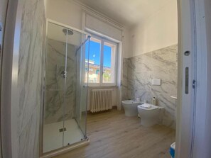 Een badkamer met een douchecabine van glas, een toilet, een bidet en een marmeren wand.