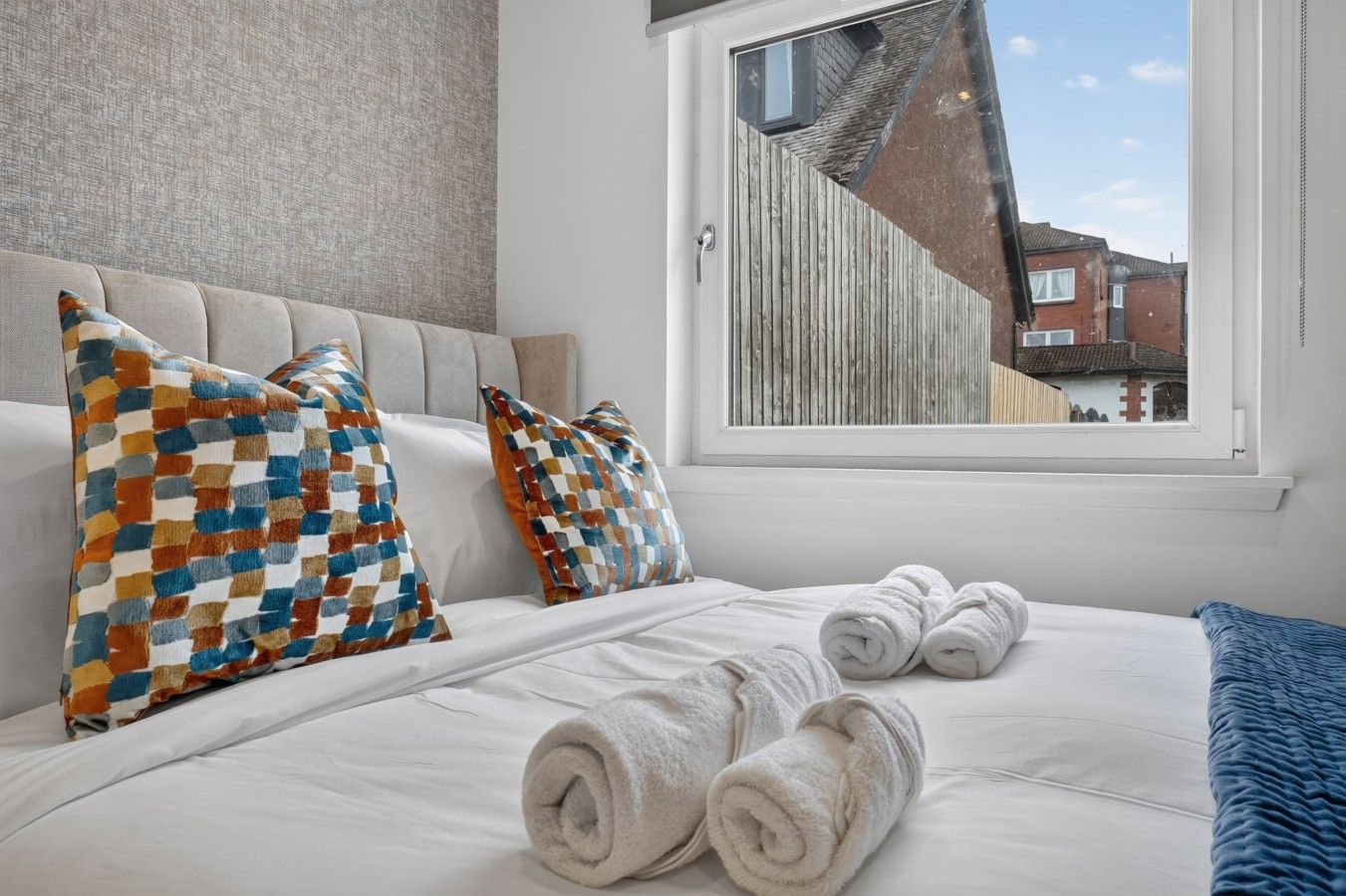 Een hotelkamer met een bed, twee kussens, een raam en uitzicht op een gebouw.