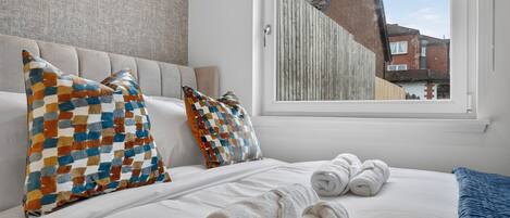 A hotel room with a bed, two pillows, a window, and a view of a building outside.