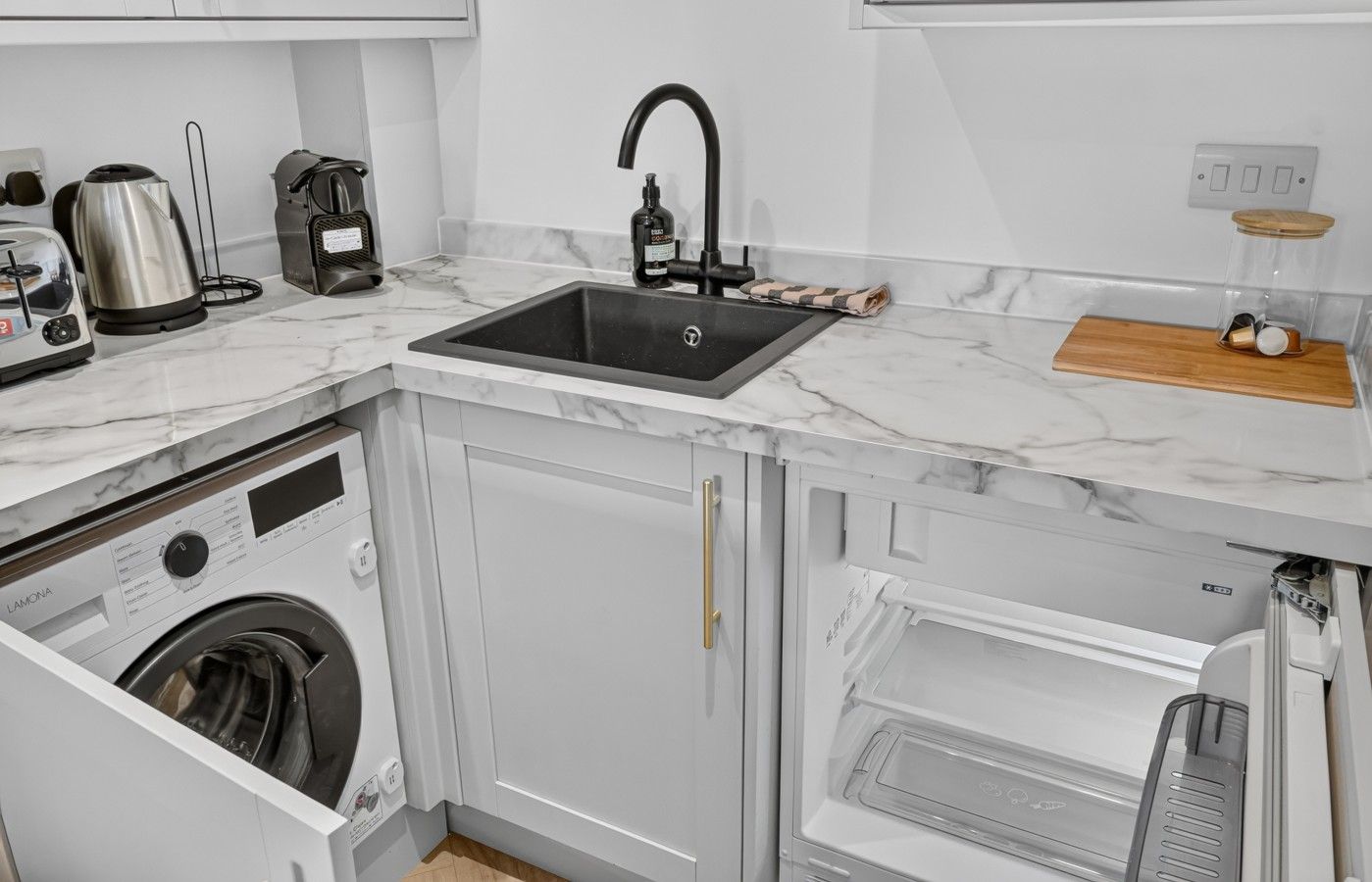 Una cocina moderna con lavadora integrada, un lavamanos y un microondas.