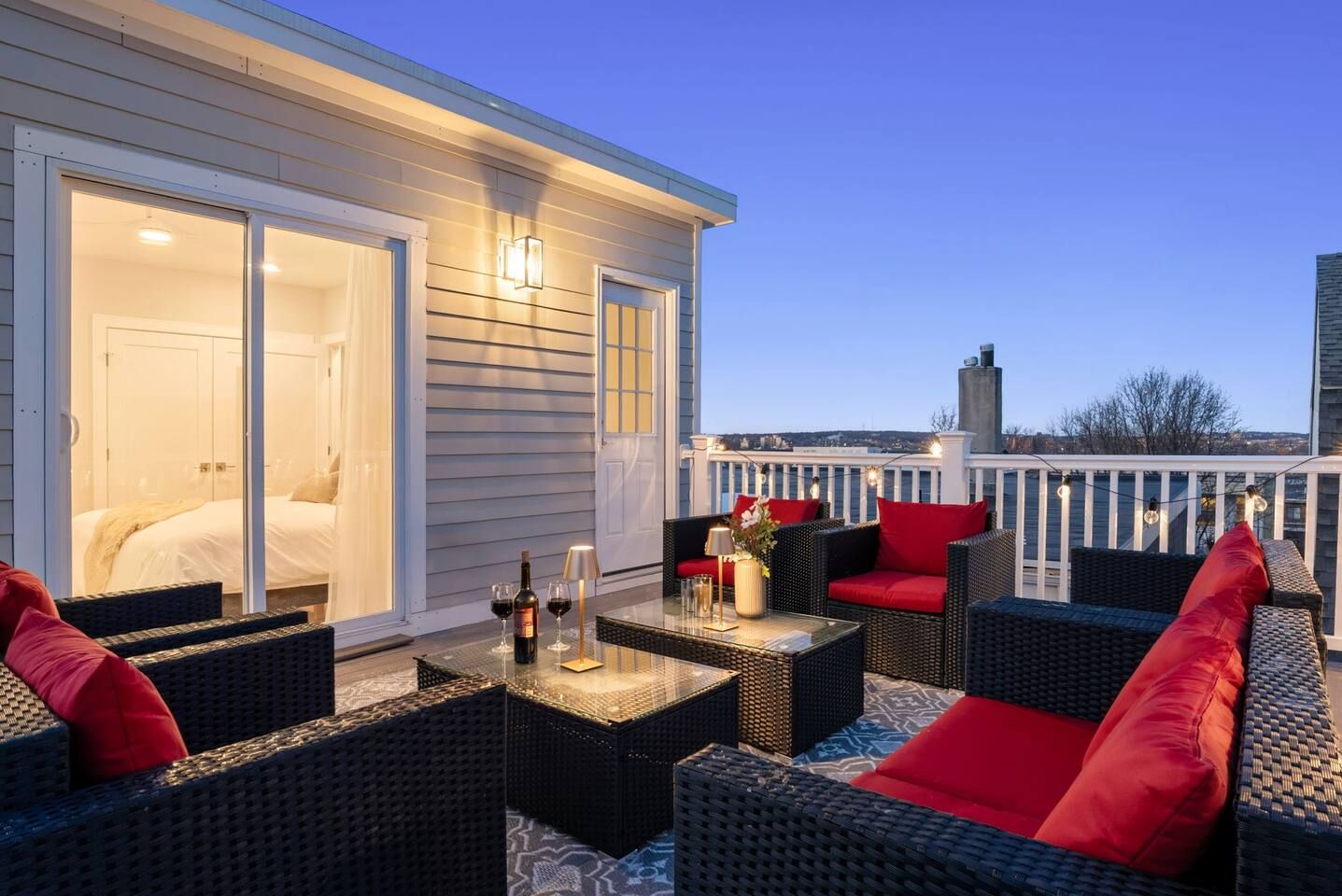 A rooftop patio with wicker furniture, a glass table, and a view of the cityscape.