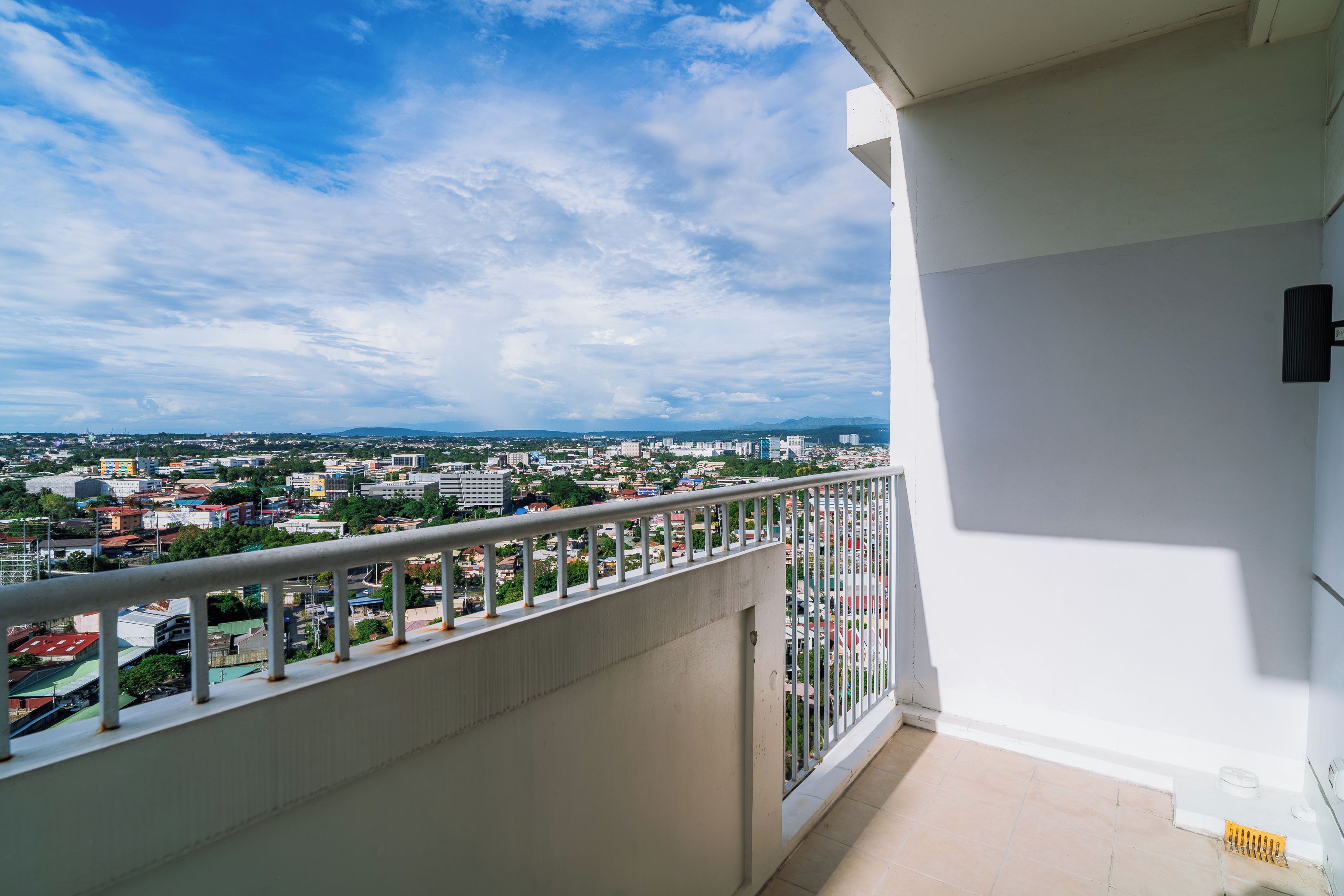 A balcony with a metal railing overlooking a cityscape with buildings and greenery.