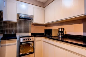 A modern kitchen with white cabinets, a stove, a microwave, and a coffee maker.