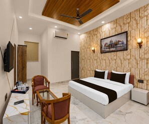 A hotel room with a bed, a desk with a chair, a television, and a painting on the wall. - Classic Hotel Shreeda (Greater Noida)