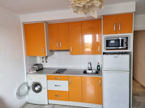 Une cuisine de taille réduite avec des meubles de couleur orange, un four à micro-ondes, un lave-linge et un évier.