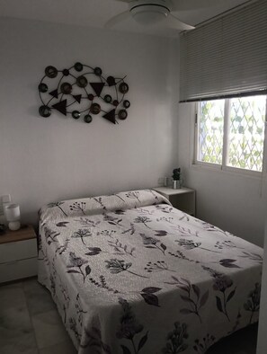 A bedroom with a bed, a wall-mounted abstract art piece, a bedside table with a lamp, and a window with blinds. - Vacation Apartment – Pool, Terrace, and Nearby Beach (Roquetas de Mar)