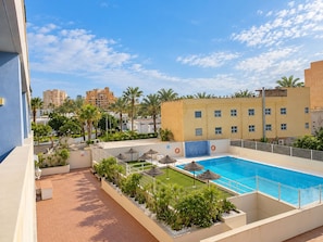 Un espace piscine aménagé sur le toit, avec une piscine à l’eau d’un bleu limpide, entourée de palmiers et d’une clôture blanche.