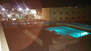 A nighttime view of a swimming pool area with surrounding buildings and street lighting. - Vacation Apartment – Pool, Terrace, and Nearby Beach (Roquetas de Mar)