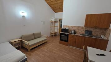 A compact kitchen with a wooden ceiling, a sofa, a dining table, and a microwave.