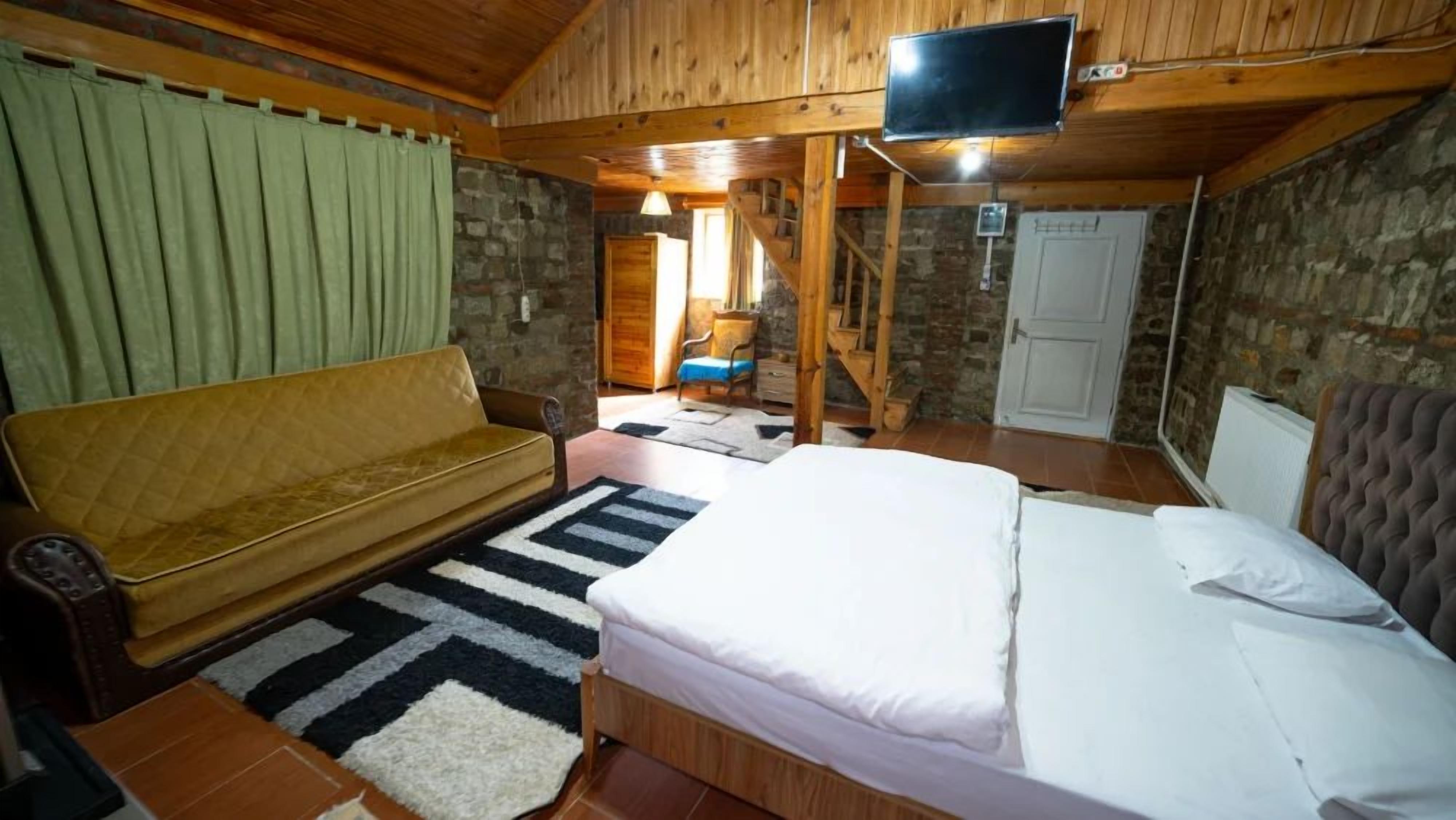 Una habitación con piso de madera, una cama, un sofá, un televisor y una escalera.