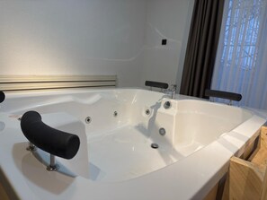 Een moderne badkamer met een witte badkuip, een zwarte kraanhendel en een houten dressoir.