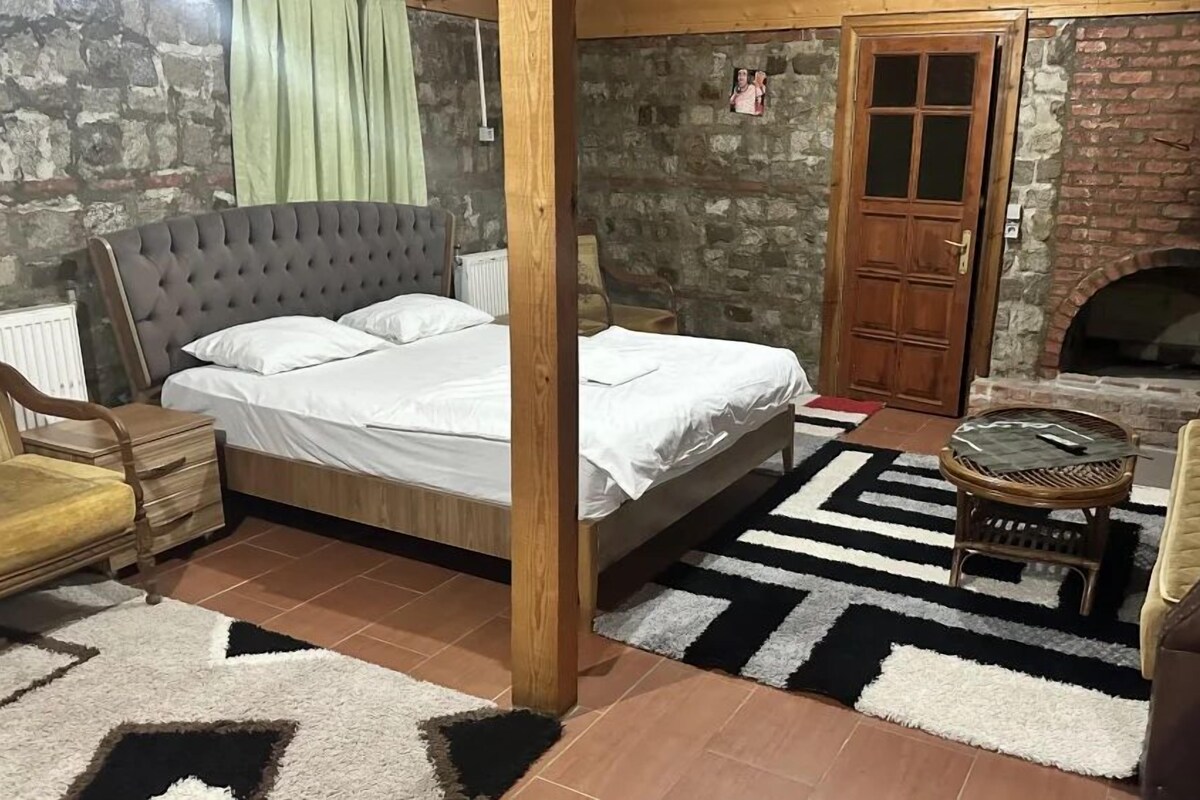 Een slaapkamer met een bed, houten hoofdbord, een bakstenen openhaard en een houten deur.