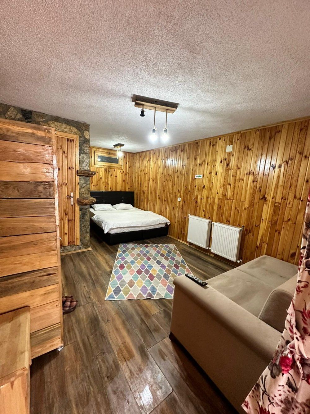 Una habitación con paredes de madera, una cama, un sofá, un tapete estampado y una lámpara en el techo.