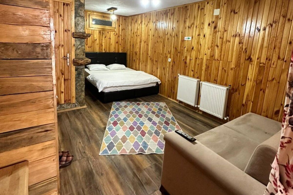Een kamer met houten wanden, een bed, een slaapbank en een vloerkleed met dessin, plus een plafondlamp.