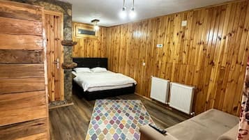 Una habitación con paredes de madera, una cama, un sofá, un tapete estampado y una lámpara en el techo.