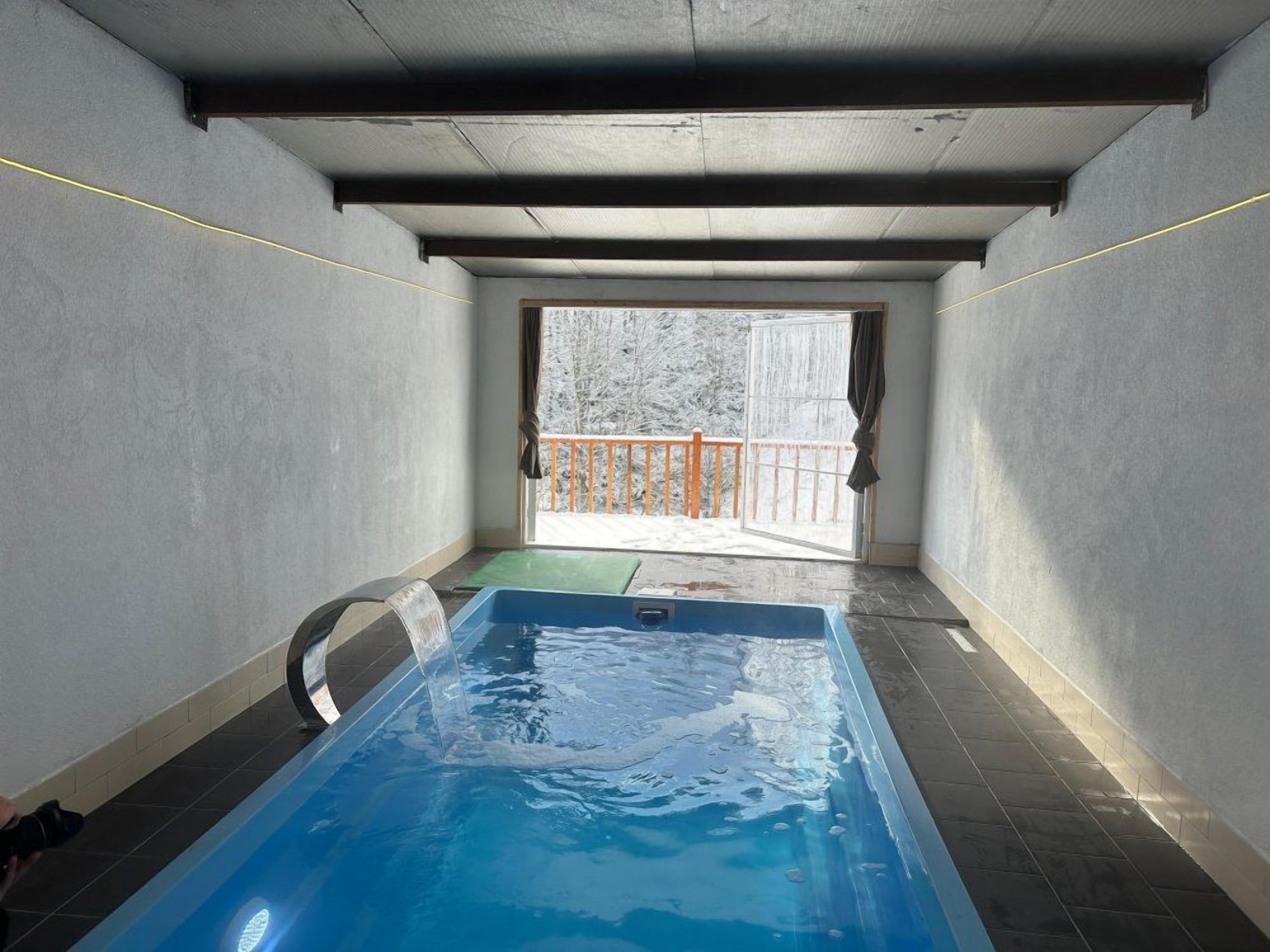 A small indoor swimming pool with a view of a snowy outdoor balcony.