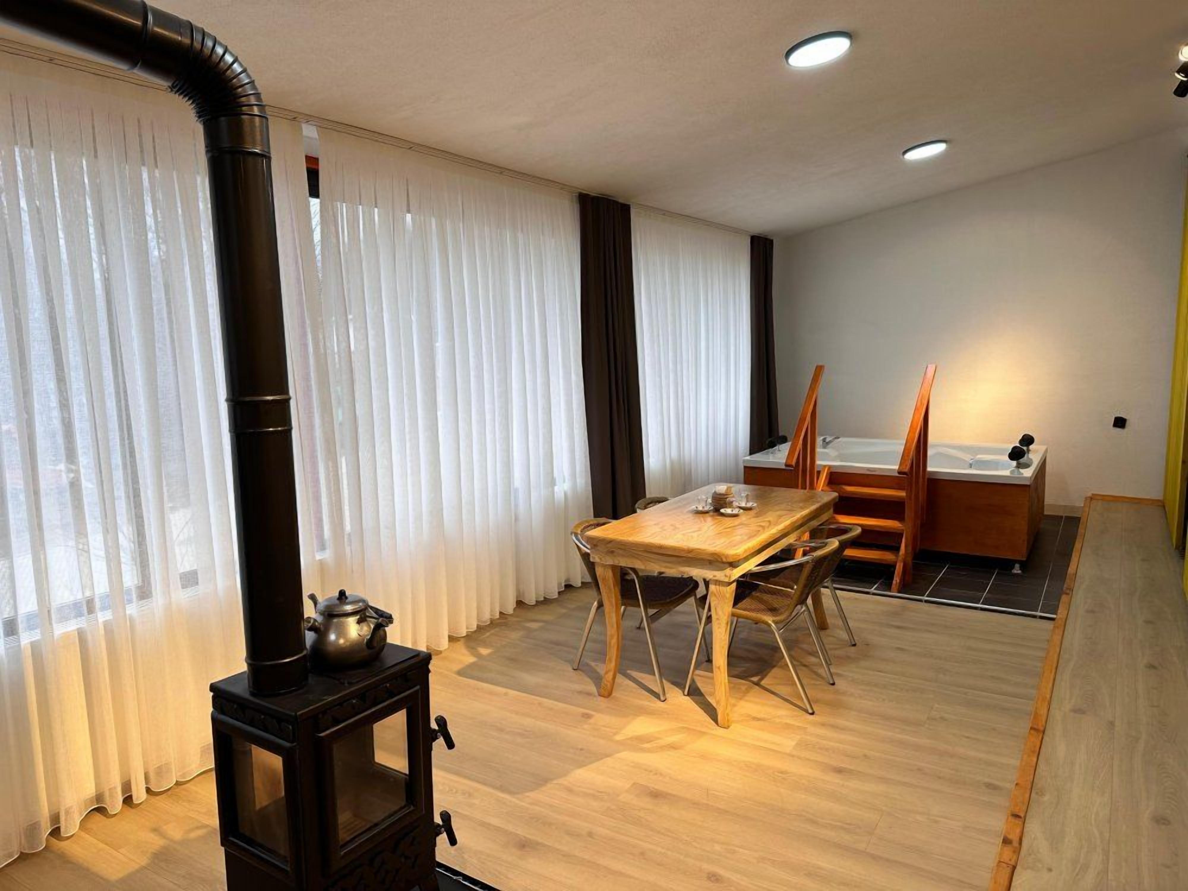 A room with a wooden table and chairs, a stove, and a window with curtains.