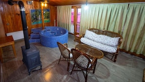 Una habitación acogedora con estufa de leña, un jacuzzi azul, muebles de mimbre y un cuadro en la pared.