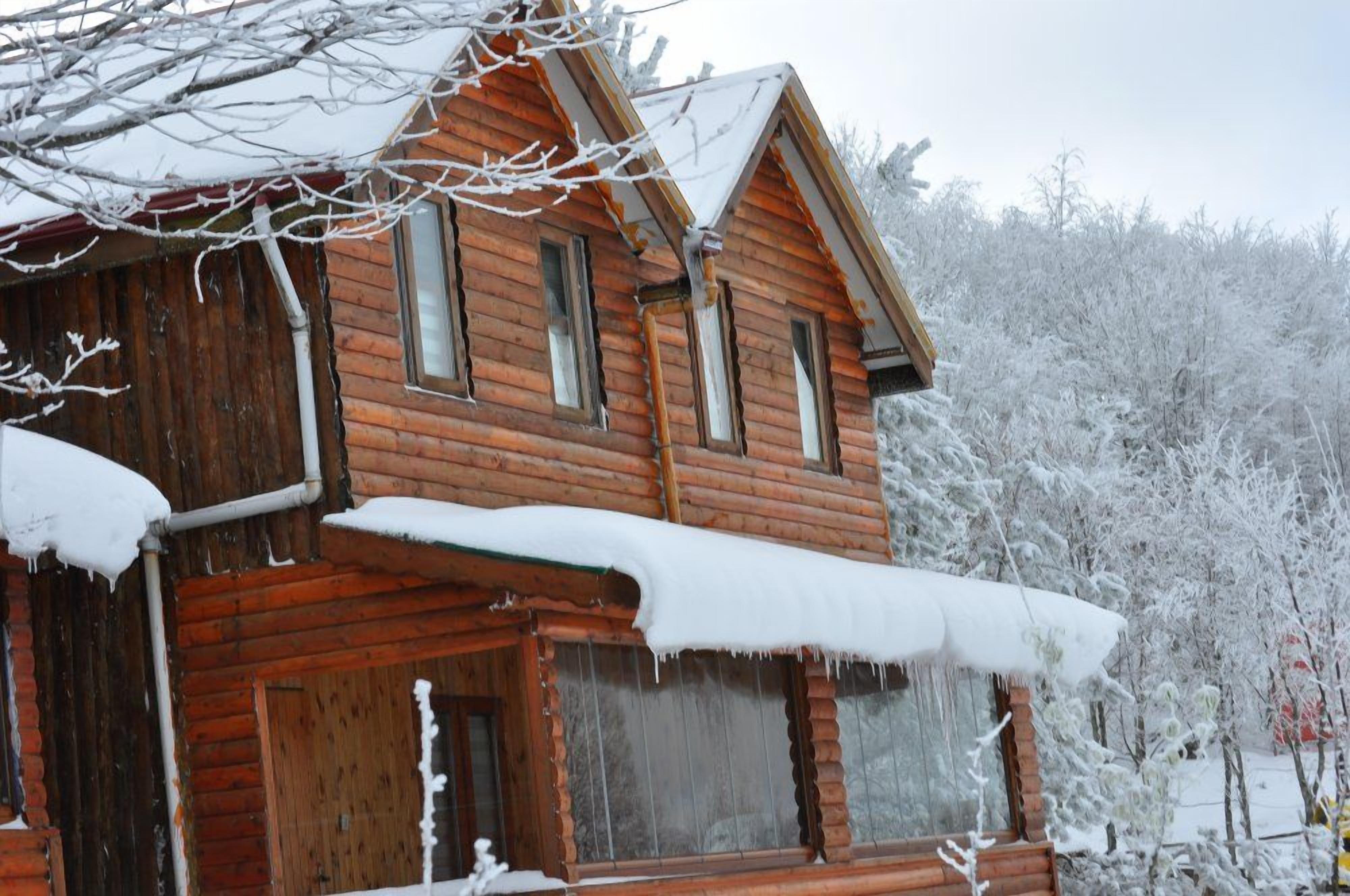 A wooden cabin with a snow-covered roof and windows, surrounded by a snowy landscape.