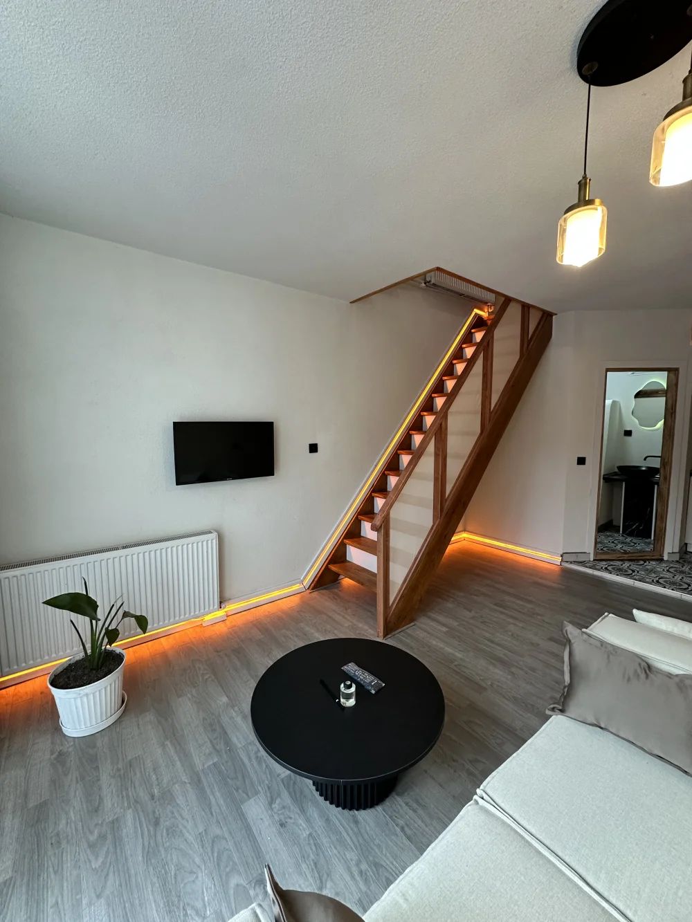 Una sala de estar moderna con una escalera de madera, una mesa de centro redonda negra y un sofá blanco.