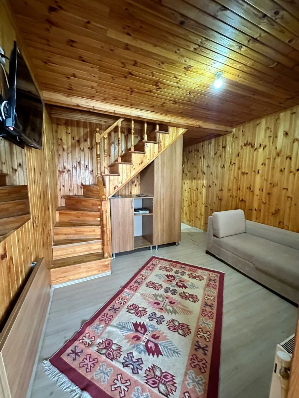 Un interior de madera con una escalera, un sofá y una alfombra estampada.