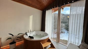 A modern bathroom with a freestanding bathtub, a wooden bench, and a large window with curtains.