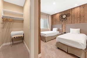 Een hotelkamer met twee bedden, een bankje, een kapstok en een houten wand met een klok.