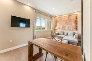 A modern living room with a wooden table, a grey sofa, and a mounted flat-screen TV. - Luxury 3BR Villa w/ BBQ Near Disney (Kissimmee)