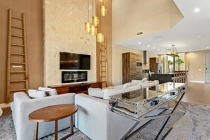 A modern living room with a large TV, a fireplace, and a kitchen area in the background. - Luxury 3BR Villa w/ BBQ Near Disney (Kissimmee)