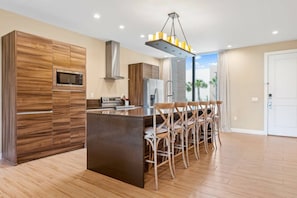 A modern kitchen with a central island, wooden cabinetry, stainless steel appliances, and a bar seating area. - Luxury 3BR Villa w/ BBQ Near Disney (Kissimmee)