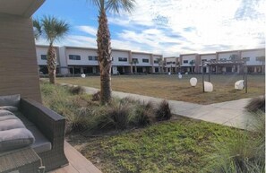 A courtyard with a modern building, palm trees, and outdoor seating. - Luxury 3BR Villa w/ BBQ Near Disney (Kissimmee)