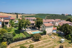 A residential area with multiple houses, a swimming pool, and a hilly landscape in the background. - Hostdomus - Pool and Wine (Rosignano Monferrato)