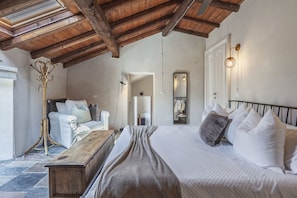 A bedroom with a wooden ceiling, a bed with white bedding, a bench, and a coat rack. - Hostdomus - Pool and Wine (Rosignano Monferrato)