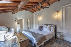 A bedroom with a bed, bedside tables, a wooden bench, and a ceiling fan. - Hostdomus - Pool and Wine (Rosignano Monferrato)