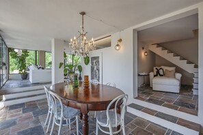 A dining area with a round table, chairs, a chandelier, and a staircase leading to a living area. - Hostdomus - Pool and Wine (Rosignano Monferrato)