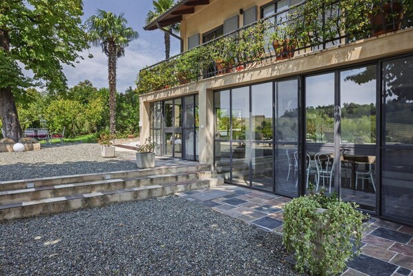 A modern building with a balcony, large windows, and a gravel driveway. - Hostdomus - Pool and Wine (Rosignano Monferrato)