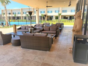 A covered outdoor seating area with wicker furniture, a statue, and a pool in the background. - Magic Village 4 Suites 8 Guests 8 min Disney (Kissimmee)