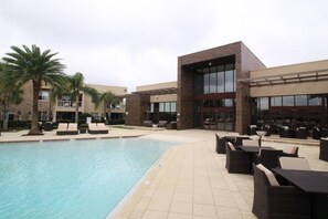 A poolside area with lounge chairs and a pool, surrounded by modern buildings with large windows and a covered patio area. - Magic Village 4 Suites 8 Guests 8 min Disney (Kissimmee)