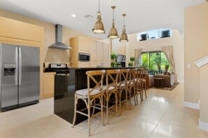 A modern kitchen with stainless steel appliances, wooden chairs, and pendant lighting. - Magic Village 4 Suites 8 Guests 8 min Disney (Kissimmee)