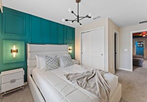 A bedroom with a large bed, teal accent walls, a white door, and a nightstand with a lamp. - Kissimmee 5BR Modern Home w/ Private Pool (Davenport)