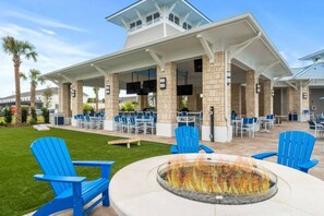 An outdoor patio area with blue Adirondack chairs, a fire pit, and a covered seating area with tables and chairs. - Kissimmee 5BR Modern Home w/ Private Pool (Davenport)