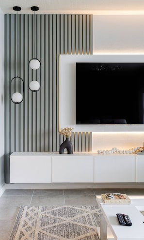 A modern living room with a large flat-screen TV mounted on a white wall, a minimalist console table below, and a patterned rug on the floor. - Kissimmee 5BR Modern Home w/ Private Pool (Davenport)