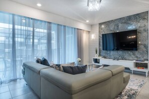 Un salon moderne avec un grand canapé, un téléviseur à écran plat fixé sur un mur en marbre et une porte vitrée donnant sur un balcon.