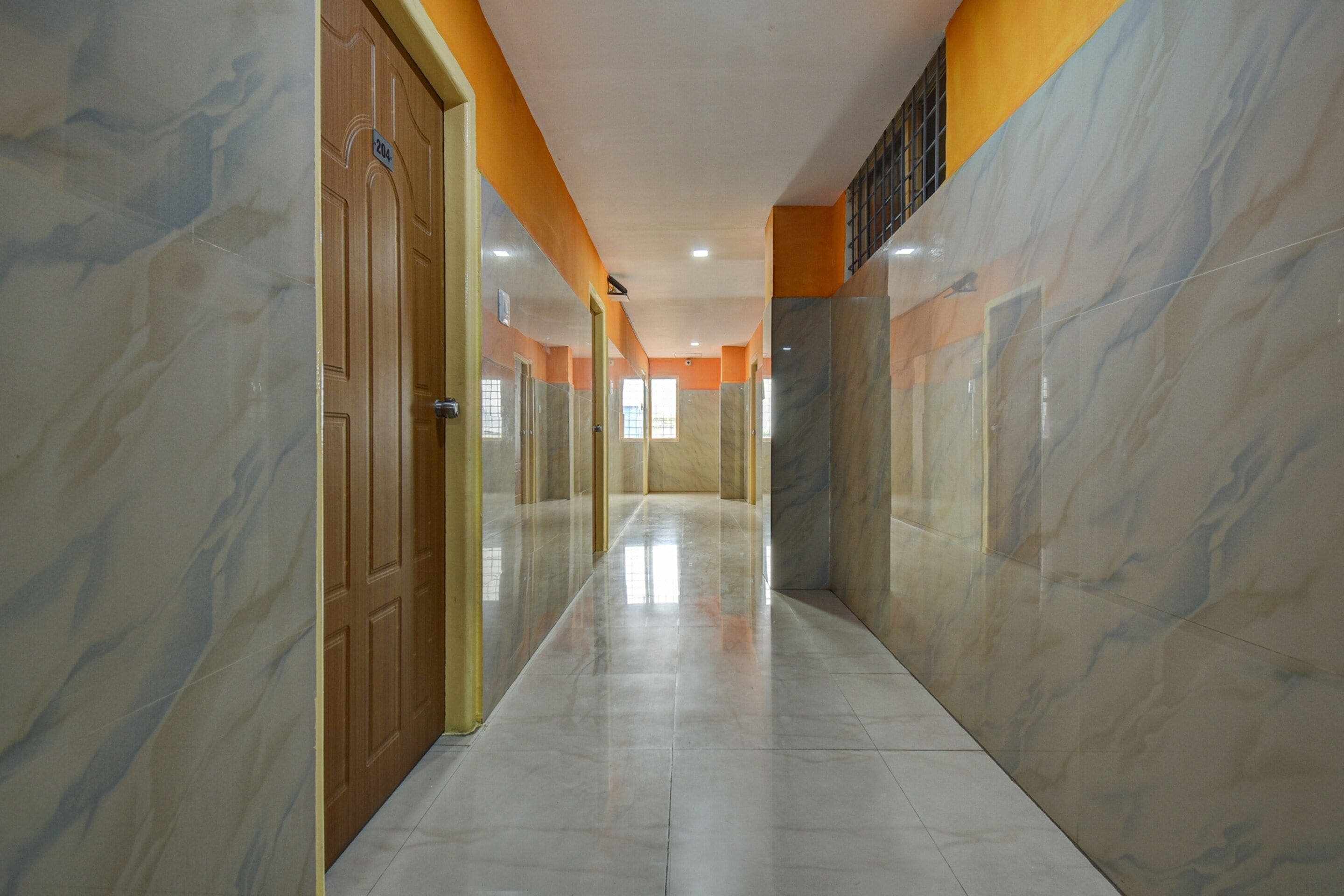 A corridor with marble walls and doors, leading to a bright room with windows.