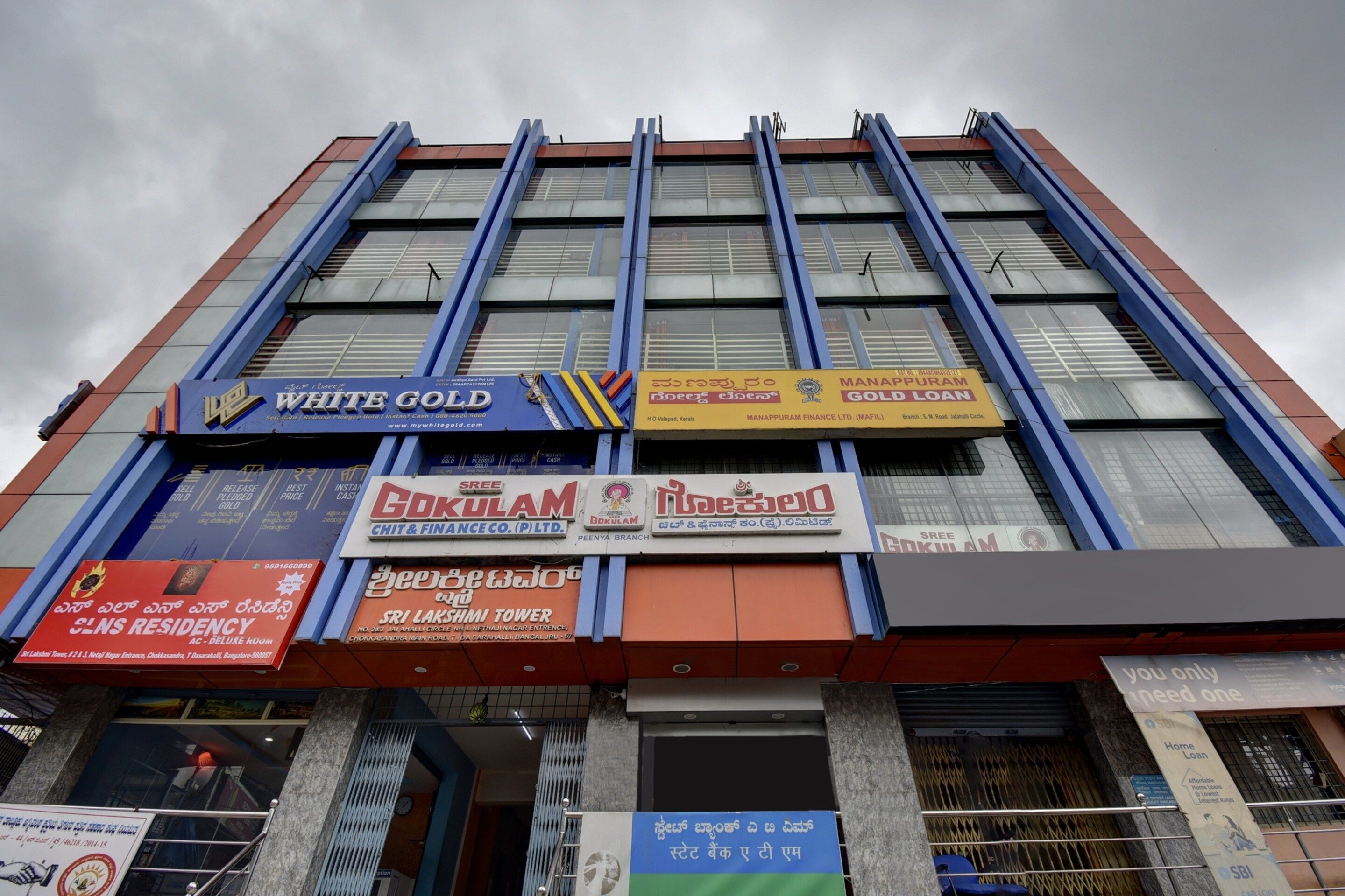 A multi-story building with various commercial establishments on the ground floor, including a bank and a gold loan company.