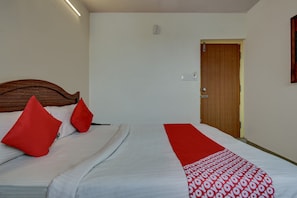 A hotel room with a bed, a wooden headboard, a red throw pillow, a white bedspread, and a red and white patterned blanket. - Hotel O K N Residency (Bengaluru)